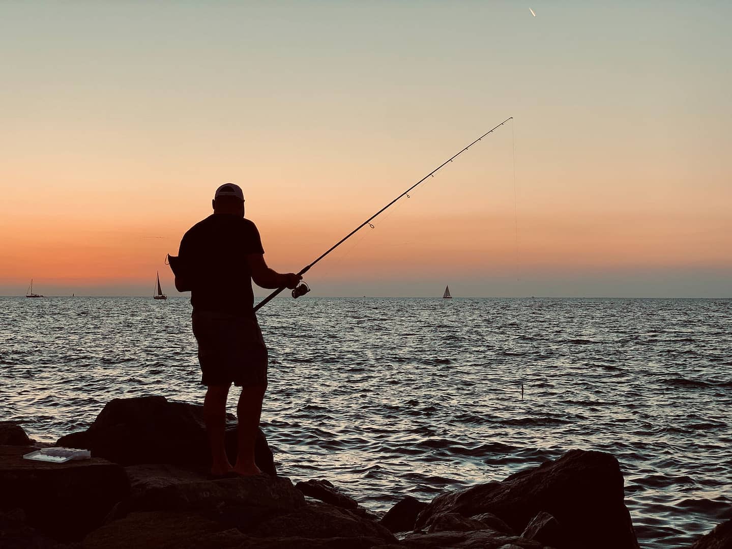 a man fishing on the rocks at sunset