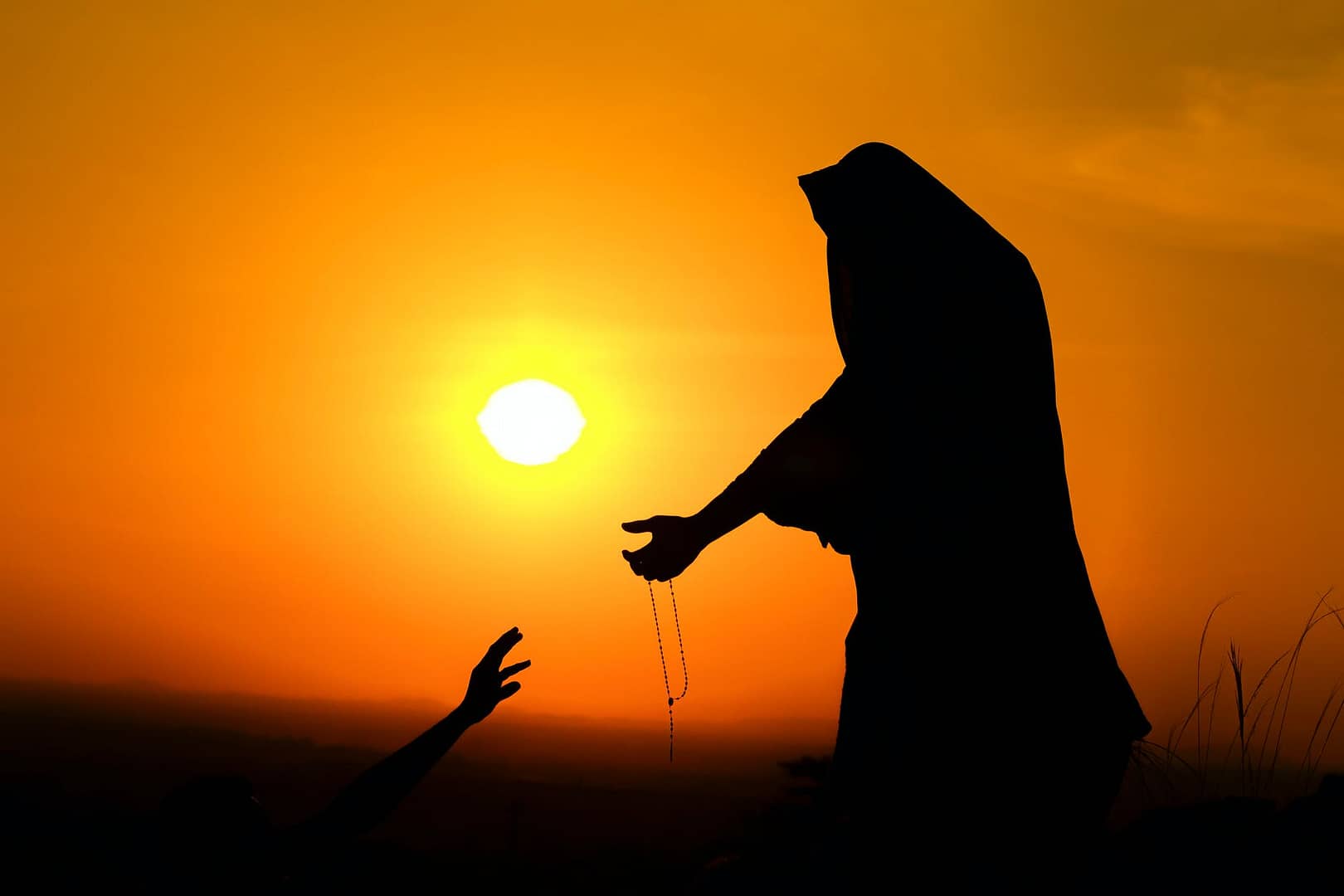 silhouette of woman outstretching hand to help man at sundown