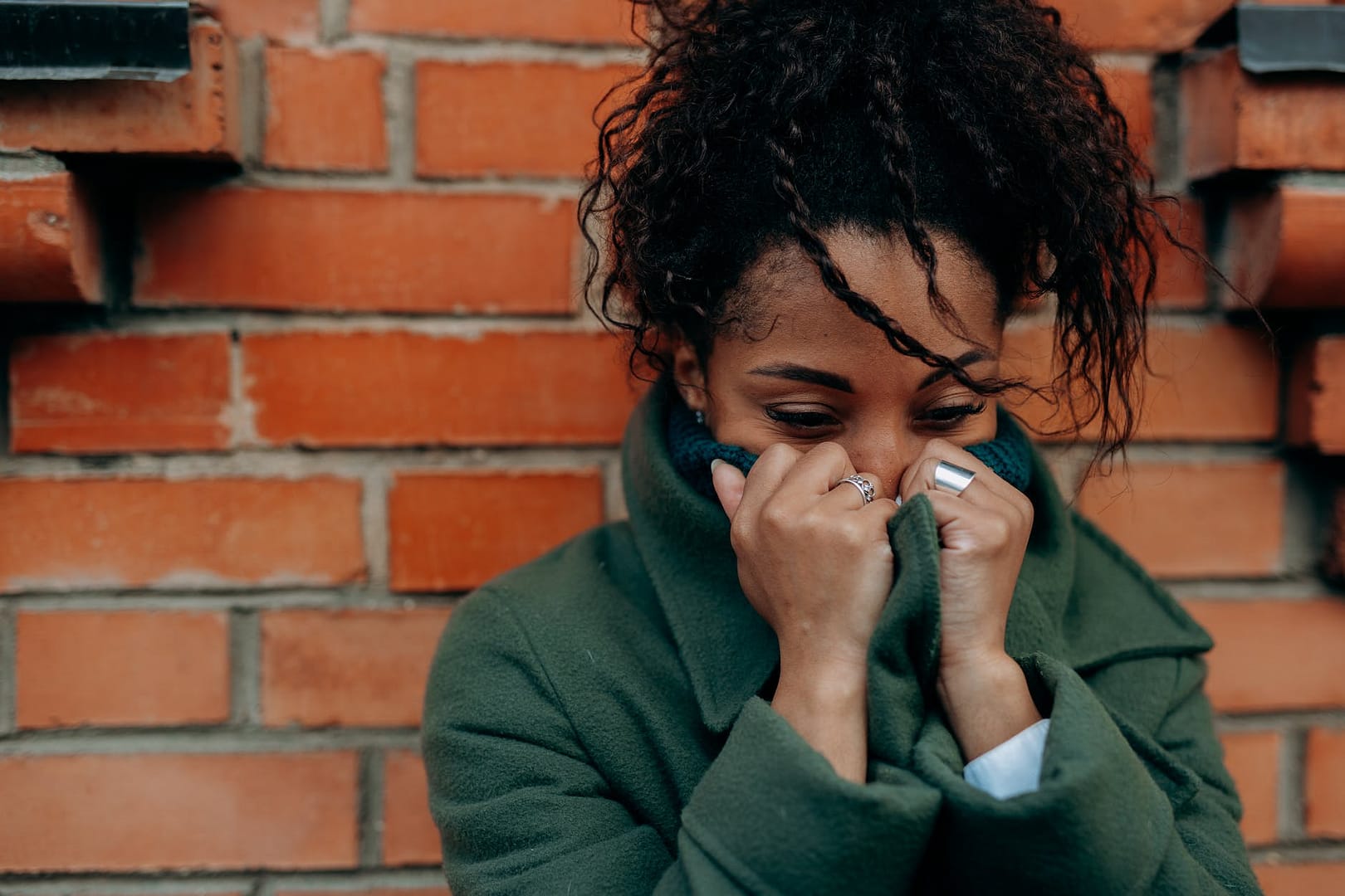 woman in green trench coat covering her face with her hands