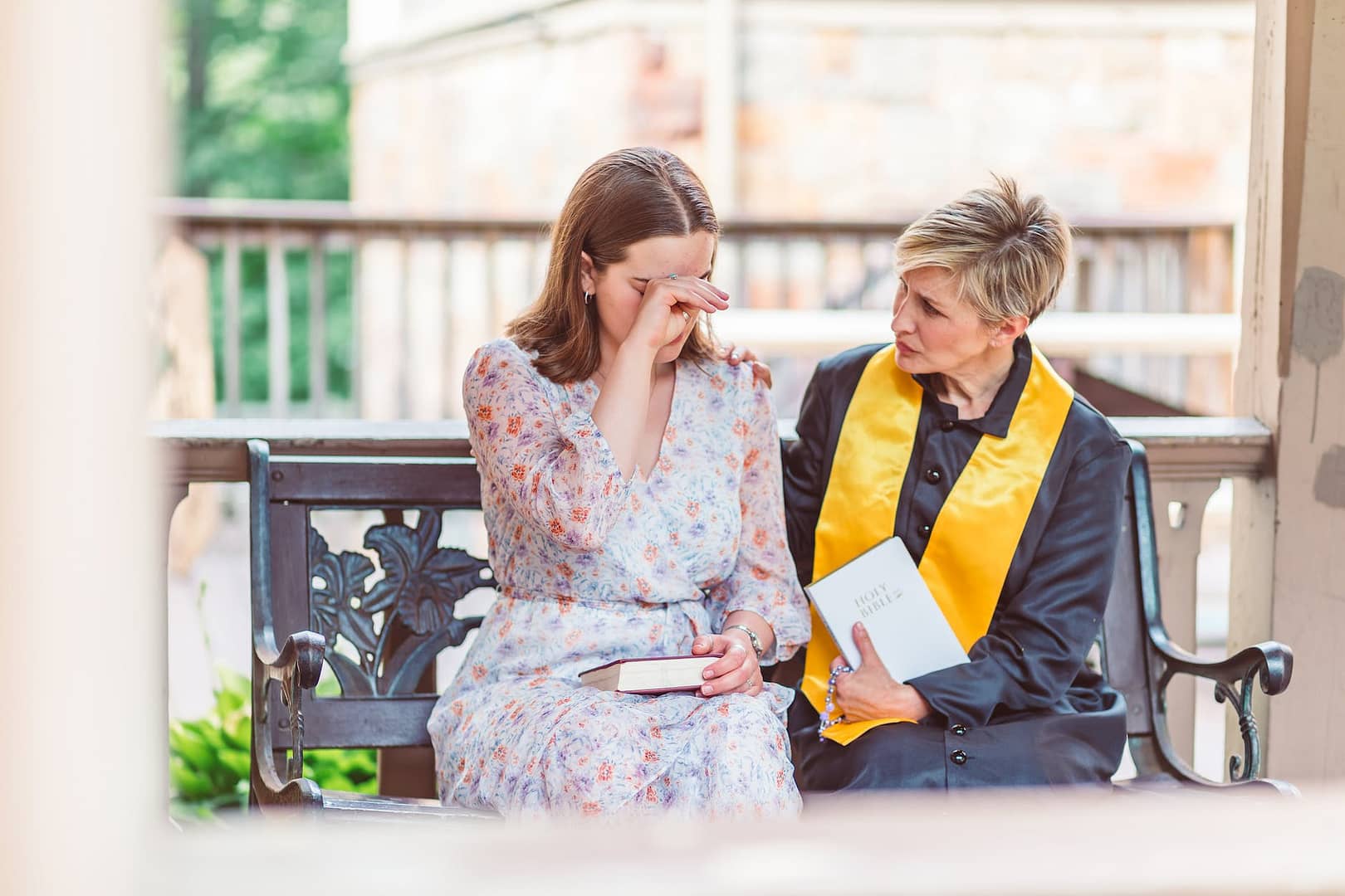 woman in white floral dress sitting on bench with a priest
